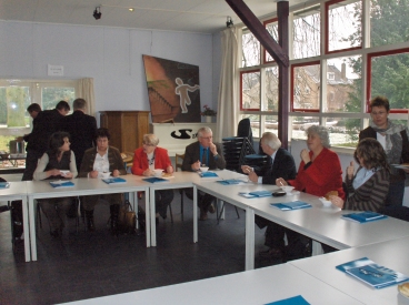 Statenleden aan de lunch tijdens een powerpoinpresentatie. Margriet Bleijenberg zit rechts in het rood.